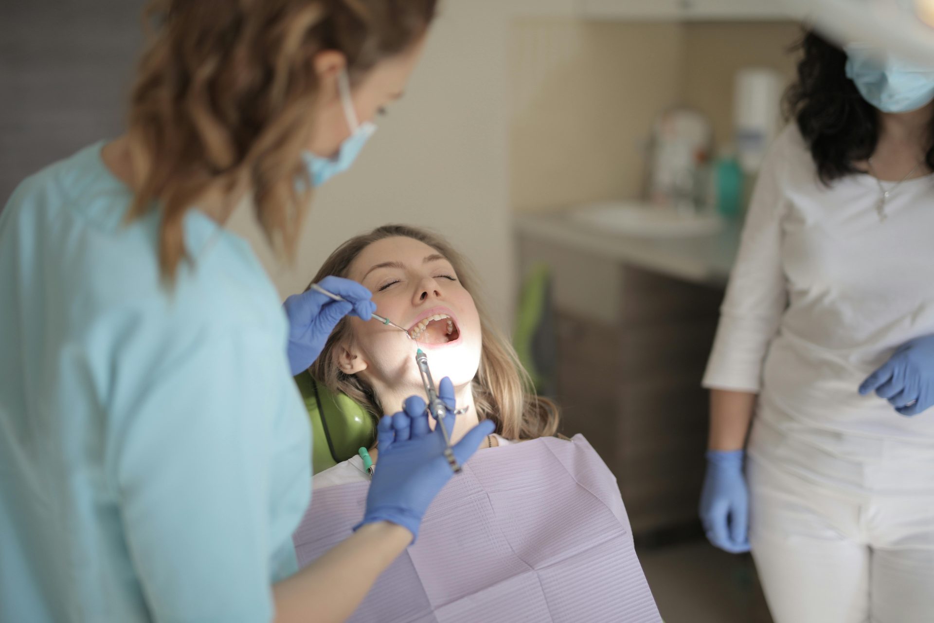 Joven odontóloga, con guantes de látex y mascarilla, aplicando una inyección mientras trata los dientes de un paciente en una clínica moderna.